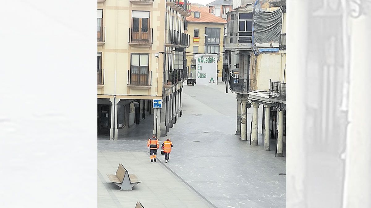 Dos voluntarios, caminando por la Plaza Mayor, vacía, de Astorga. | L.N.C.
