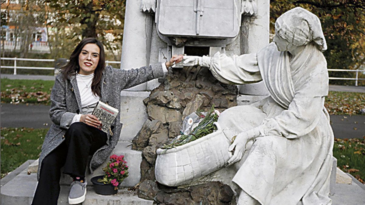 Aitana Castaño con su libro en una mano mientras extiende la otra para coger la de la escultura dedicada a las carboneras en Sama de Langreo.