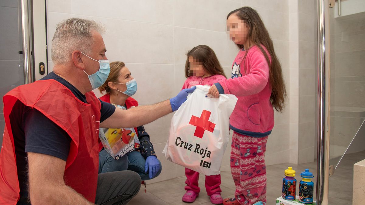 Dos voluntarios de Cruz Roja entregan varios juguetes a dos niñas. | L.N.C.