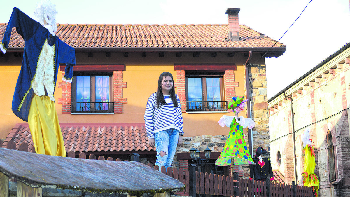 Ana Pérez Díez, Anina, en el muro de la plaza de la Iglesia de Cármenes rodeada de algunos de los disfraces que ha colocado.