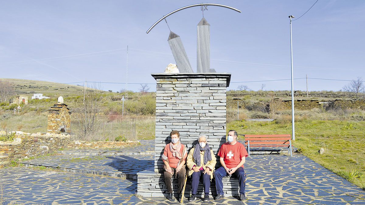 Isabel García Rodera, Aurea San Román y Francisco José Sanromán sentados ‘a la sombra’ del monumento al relojero en su pueblo. | FULGENCIO FERNÁNDEZ