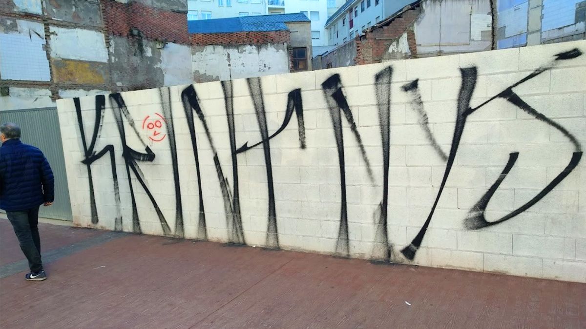 Una de las pintadas, en un vallado de una céntrica calle de la ciudad, con ruinosos edificios al fondo.