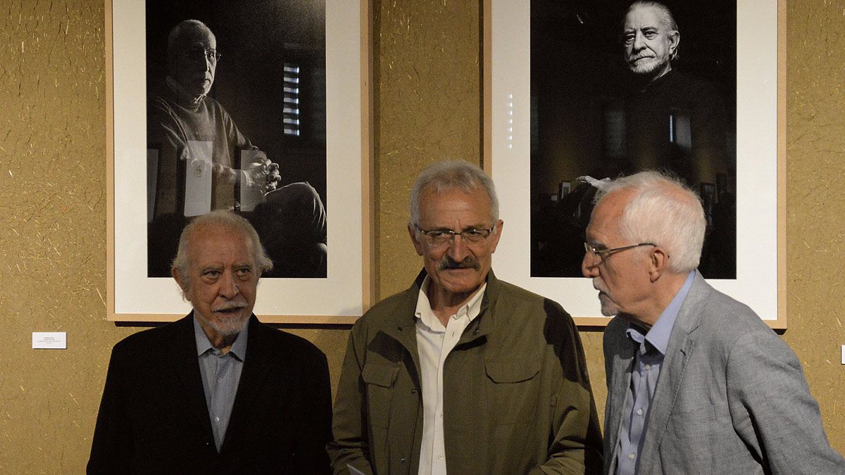 José María Merino y Luis Mateo Diez charlan con el alcalde de Gordoncillo, Urbano Seco, delante de dos retratos de los escritores. | F. FERNÁNDEZ