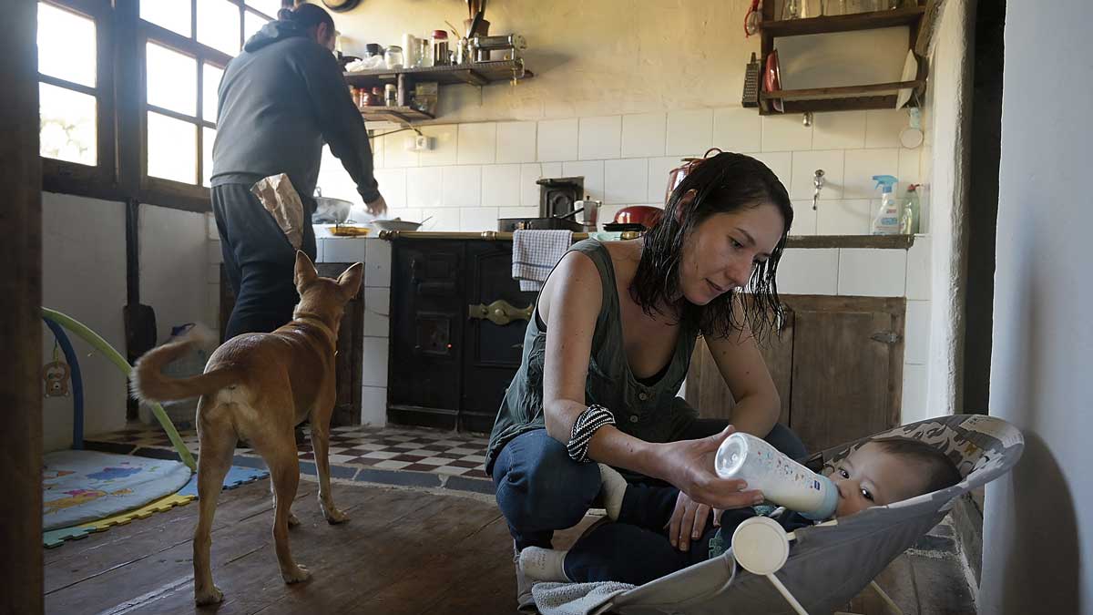 Isabel Bailey le da el biberón a Alejandro mientras Fede Bayo prepara la comida en la cocina de la casa que han arreglado en Santalavilla. | REPORTAJE GRÁFICO: JESÚS F. SALVADORES