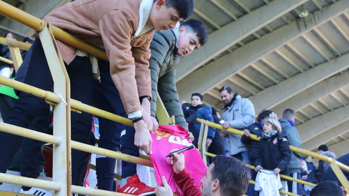 Castañeda firma una bandera de León a dos jóvenes seguidores. | CYD