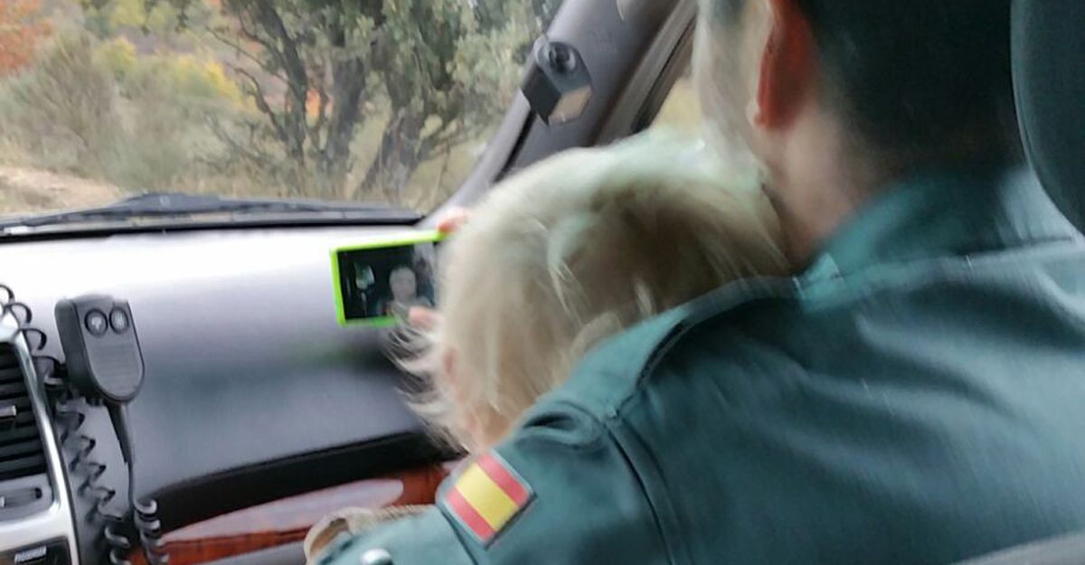 Un agente sostiene al pequeño en el coche patrulla tras encontrarlo en una pista forestal en buen estado.