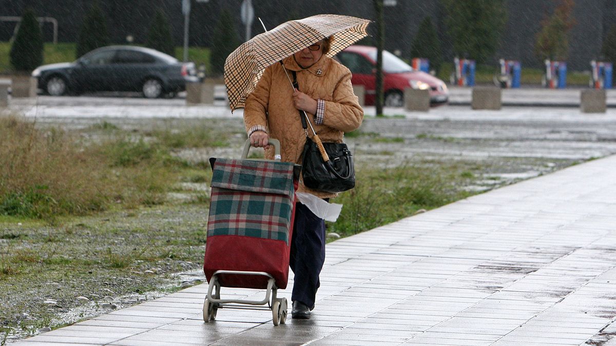 Una mujer se cobija del intenso viento y la lluvia en Ponferrada. | CÉSAR SÁNCHEZ (ICAL)