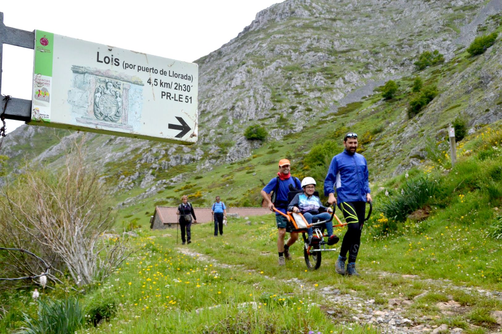 Una mujer realiza la ruta de la Llorada de Lois subida en una silla jölette y empujada con ayuda de dos compañeros senderistas. | MARCE FERNÁNDEZ