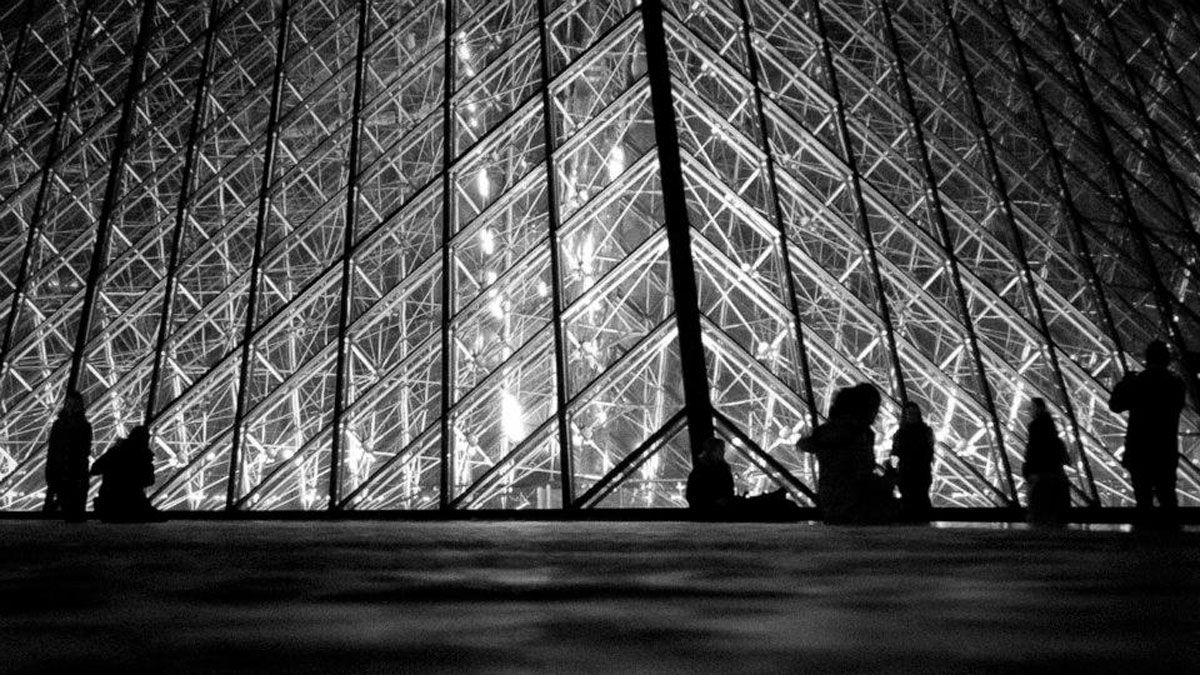 Siluetas junto a la pirámide de cristal del Museo del Louvre de París, iluminada por la noche. | PABLO J. CASAL