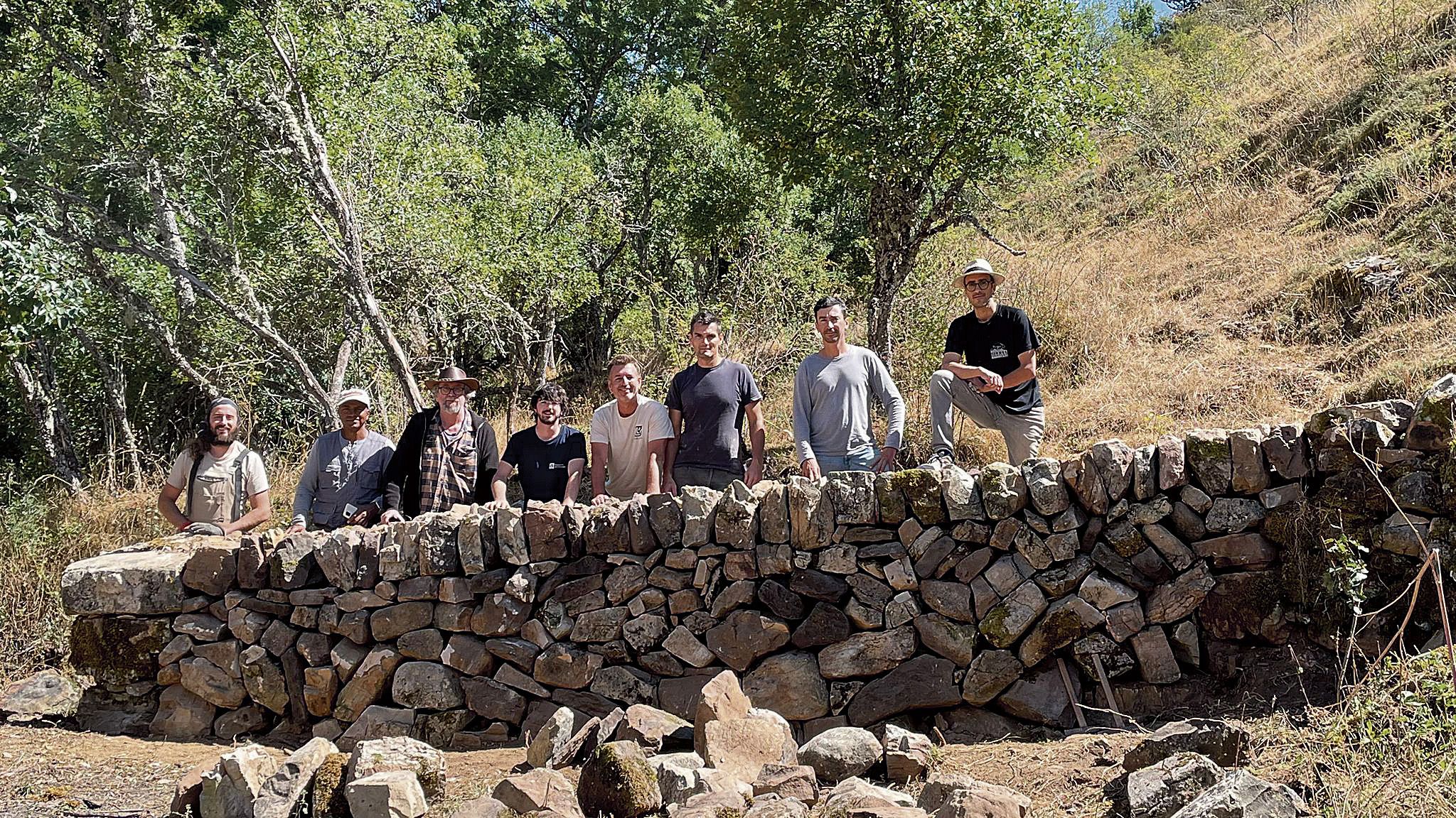 Los participantes en el taller de Pared con piedra seca posan detrás de la obra que da fe de la utilidad del curso celebrado en Rodrillazo esta pasada semana | César Prieto 