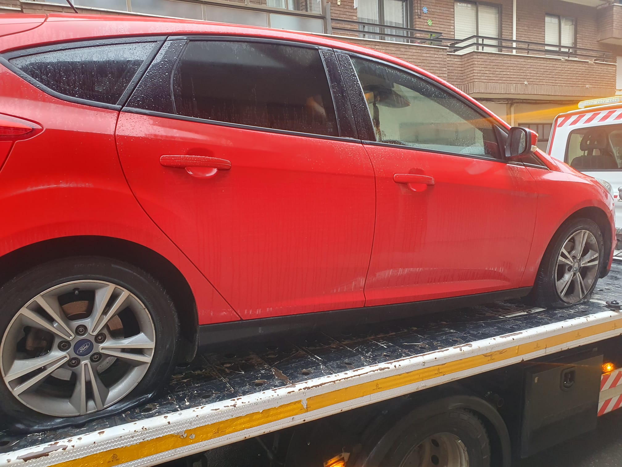 Coche siendo llevado en grúa con las ruedas pinchadas.