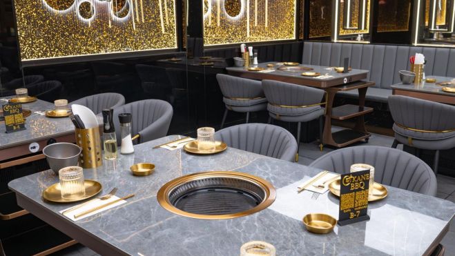 Imagen del interior de Okane BBQ con las planchas para cocinar en el centro de la mesa Imagen del interior de Okane BBQ con las planchas para cocinar en el centro de la mesa