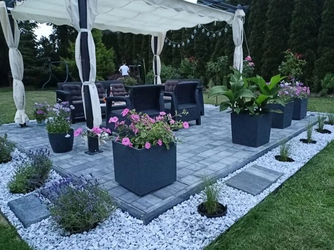 Cenador de jardín con cortinas sobre una terraza de adoquín con conjunto lounge y maceteros con flores