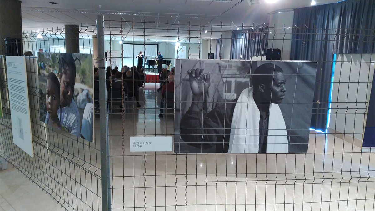 Un fragmento de la exposición ’Somos migrantes’ y, al fondo, público y concierto de Siringe. | P. FERRERO