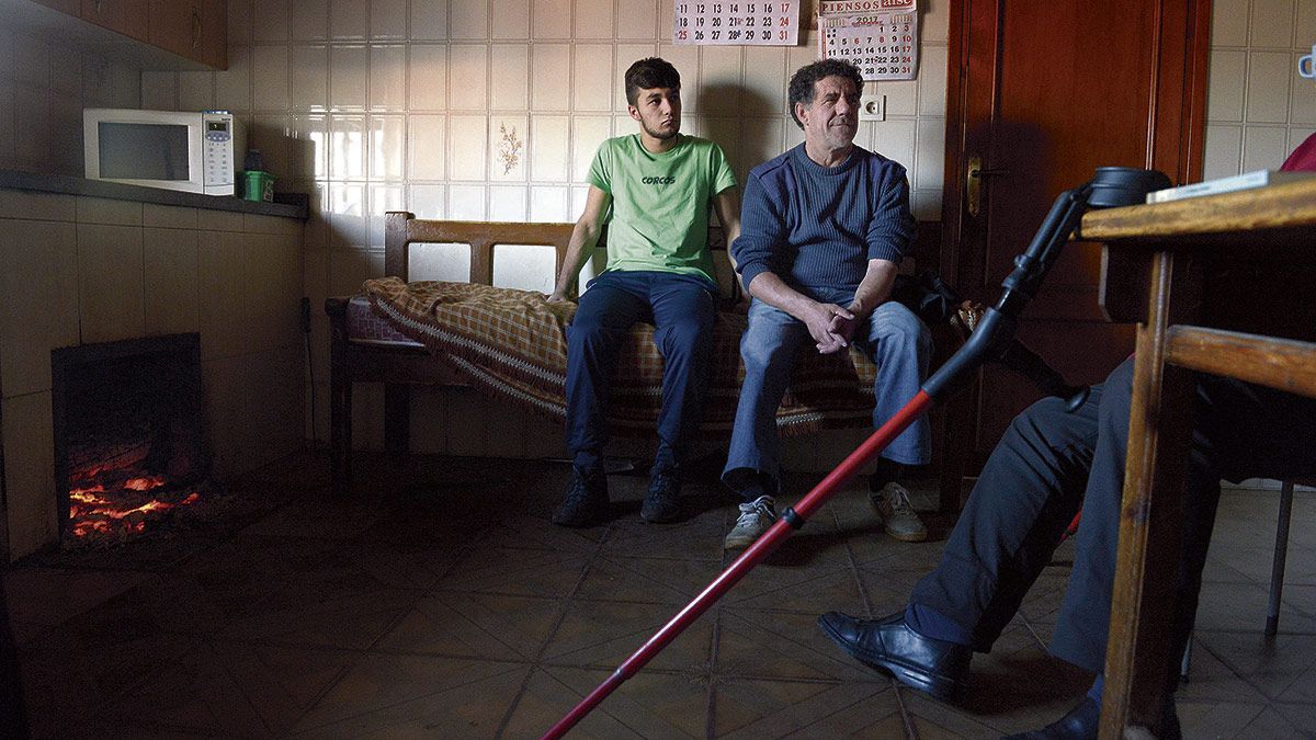 Daniel Cerezal sentado en el escaño de su casa de Corcos junto a su hijo Rubén, al calor de la lumbre que atiza su madre, Asunción. | MAURICIO PEÑA