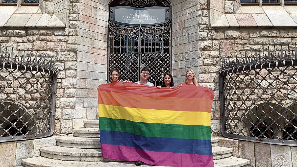 Cuatro jóvenes con la bandera del arcoíris en la fachada de la Casa Botines.