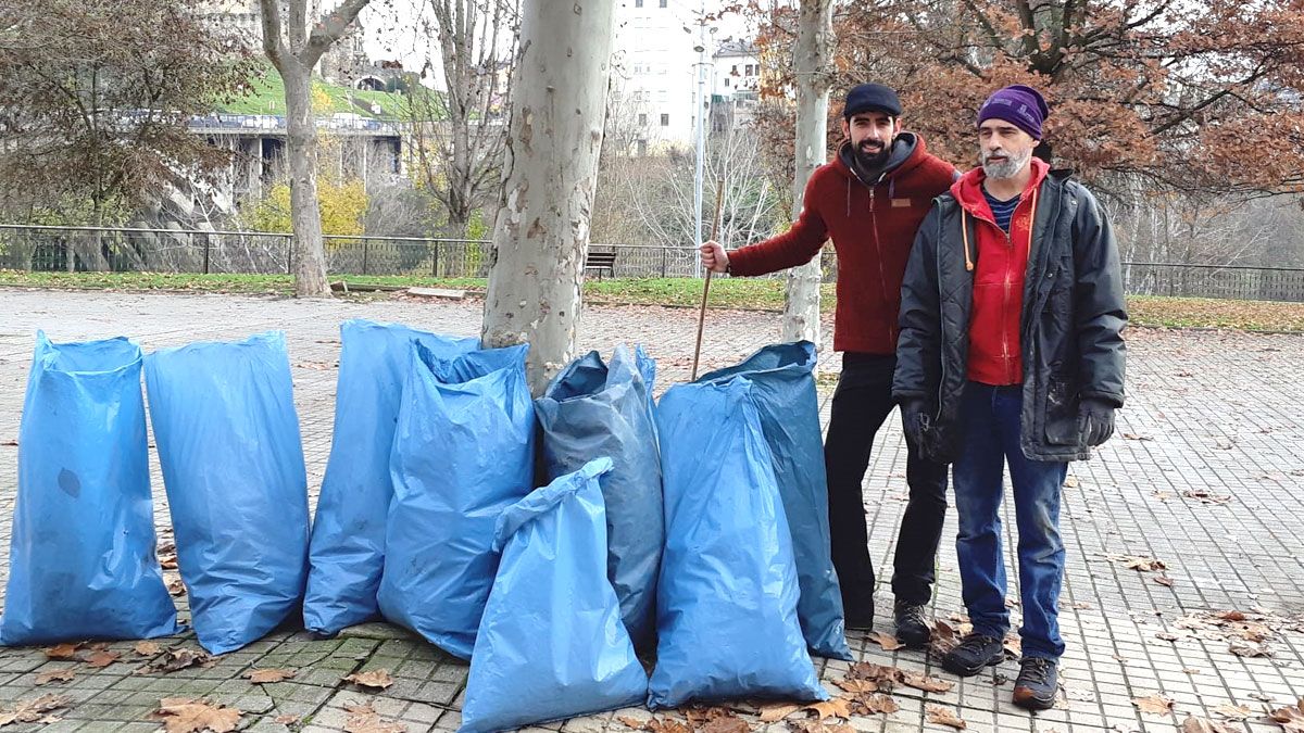 Dos de los activistas posan este lunes con los sacos de basura recogidos en las orillas del río Sil, en el entorno del mercado ambulante.| P.O.