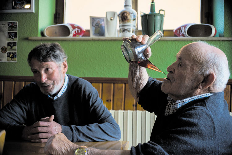 Camilo del Molino, Chile, bebe del porrón bajo la atenta mirada de Modesto Muñiz, Sancho, en el bar de Josu (El Riosol) en Maraña.| MAURICIO PEÑA
